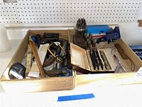 Photo showing a box with assorted hand tools including tape measure, hammers, saws, clamps, drill bits, and tape measure.