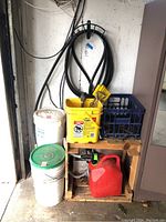 Photo showing items stored on wooden shelves including red gas can, coiled hose, yellow container, and blue plastic crate in garage.