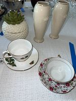 Lenox vases, tea cups with saucers, lidded pineapple jar, green succulent decorative item on table