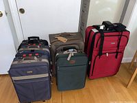 Photo showing five pieces of luggage on a wooden floor: three navy and brown Jaguar-branded suitcases, one green, and one large red suitcase.