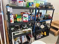 Three black plastic shelving units holding various garage and household items.