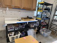 Photo of black plastic shelving units in garage setting with various storage bins and boxes on and around them.