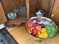 Silver tone serving bowl filled with assorted faux fruit on wooden floor