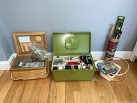 Wide view of all sewing and knitting materials including wooden box, green metal box, basket, and yarn container