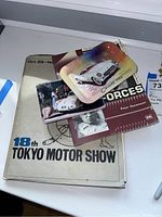 Full lot overview showing Tokyo Motor Show booklet, Nissan photos, Corvette trinket dish, postcards, and Driving Forces book.