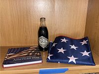 Full view of the vintage Coca-Cola bottle, the folded American flag, and the Americana book placed on a wooden surface.