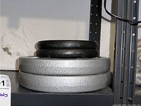 Stack of four barbell weight plates: two smaller black 10 lb plates on top of two larger silver 25 lb plates.
