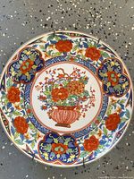 Top view of the round antique Imari plate showcasing detailed floral and geometric hand-painted designs in red, blue, green, and gold tones.