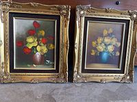 Pair of flower paintings side by side, showing full framed artwork in ornate gold-tone carved frames.