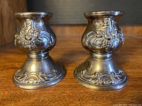 Pair of silverplate Baroque style candle holders by Wallace, showing front decorative detail and shape.