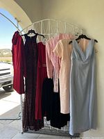 Group photo of six evening and special occasion dresses hung on a white metal rack, showing variety in color and style.