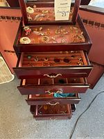 Full view of several drawers of a wooden jewelry box containing various jewelry pieces on pink lining, showing the full collection in the lot.