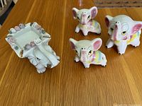 Four midcentury ceramic elephant figurines arranged on a wooden surface showing front and angled views. One elephant holds a planter area on its back with molded pink roses.