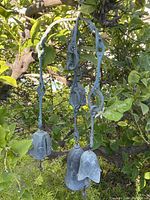 Full view of the outdoor metal windchime hanging among tree branches, showing entire structure with three bell chimes and the arch-shaped frame.