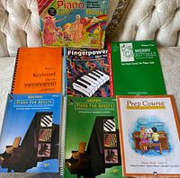 Photo of seven piano instructional books arranged on a sofa showing the titles and colorful covers.