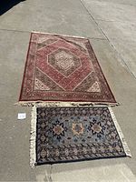 Two floor rugs displayed on concrete ground, showing full view of both rugs with respective size tags near each rug.