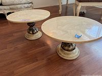 Pair of midcentury round side tables with beige marble tops on ornate round metal bases showing slight base separation on one table.