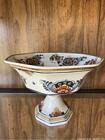 Side angle showing the bowl's shape, footed base, and detailed floral design with gold rim on wooden background.