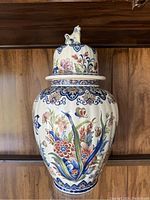 Full front view of the ceramic vase showing floral patterns and lid with animal figurine.