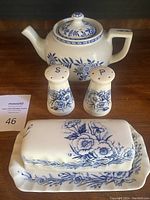 Full set showing teapot, butter dish with lid, and salt & pepper shakers, all featuring blue floral decoration on cream-colored ceramic.