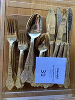 Photo of full set with gold electroplated knives, forks, spoons arranged in a clear tray, showing detailed pattern on handles.