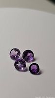 Four round faceted amethyst gemstones in deep purple shade on plain white background arranged in group