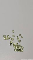 Multiple small apple green Peridot gemstones spread on a white surface showing their round diamond cut facets and light green color.