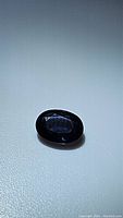 Oval cut blue sapphire gemstone shown on white background under diffused light, highlighting the deep blue color and oval shape.