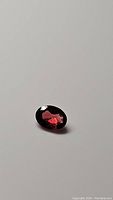 Oval cut garnet gemstone laid flat showing deep cherry red color with light reflections on facets.