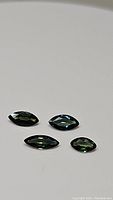 Four marquis cut natural sapphires in varying blue-green colors laid out on a white surface.