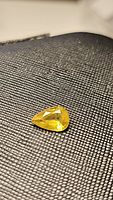 Close-up image of a natural golden yellow sphene gemstone with a pear cut placed on textured black fabric.