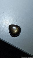Photo of a 3.29ct black star sapphire cabochon showing the dark color and the partial star asterism on the polished surface.
