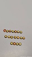 Photo showing 18 round cabochon sapphires arranged in three rows, varying slightly in yellow to orange hues, well-polished and round. Sizes approx 2.2-2.3mm.