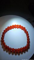 Photo of natural carnelian bead stretchy bracelet on neutral light background, showing vibrant fire orange color of beads and circular shape of the bracelet.