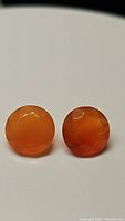 Pair of round faceted natural mandarin orange carnelian gemstones on a white background, showing the color and natural banding.