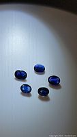 Top view of five deep blue oval cut sapphires arranged in a group showing their color and shape under focused lighting.