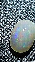 Close-up image of the natural Ethiopian opal cabochon showing rainbow flashes on a textured background.