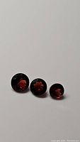 Three round faceted cherry red garnet gemstones, diamond cut, shown together on white background to display color and cut.
