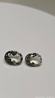 Pair of oval cut natural green amethyst gemstones shown from top angle with faceted surfaces visible.