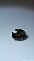 Close-up photo of oval cut sapphire showing dark blue-green colors and faceting.