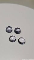 Four natural round cabochon purple iolite gemstones on a light background showing their translucent quality and inclusions.