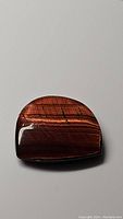 Polished natural red tigerseye fancy cabochon gemstone displaying rich reddish-brown color and chatoyancy on a white background.