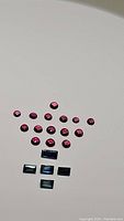 Photo showing 14 round cabochon deep red-pink raspberry sapphires and 5 baguette cut blue sapphires arranged on a flat surface.