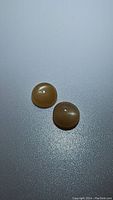 Pair of two round cabochon peach moonstones placed on flat surface showing light peach translucent color and surface flash.