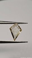Close-up image of a fancy kite-shaped transparent citrine with golden needle rutile inclusions held by tweezers, showing the checkerboard cut facets.