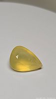 Close-up photo of the pear-shaped natural yellow Mexican opal gemstone on a plain background showing its color and cut.