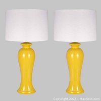 Pair of yellow glazed pottery lamps with white drum shades shown side by side against a neutral background.