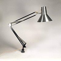 Side profile view of the lamp fully extended showing articulating black metal arm with brushed aluminium conical shade and clamp base mount.