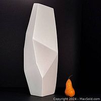 Front view of the tall white asymmetrical faceted pottery vase, showing the polygonal facets with a pear placed beside for scale.