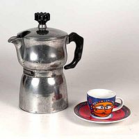 Photo showing vintage aluminum Italian espresso maker with black handle and knob alongside colorful Ritzenhoff espresso cup and saucer.